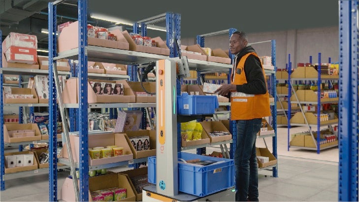 man picking items in a warehouse with a cobot